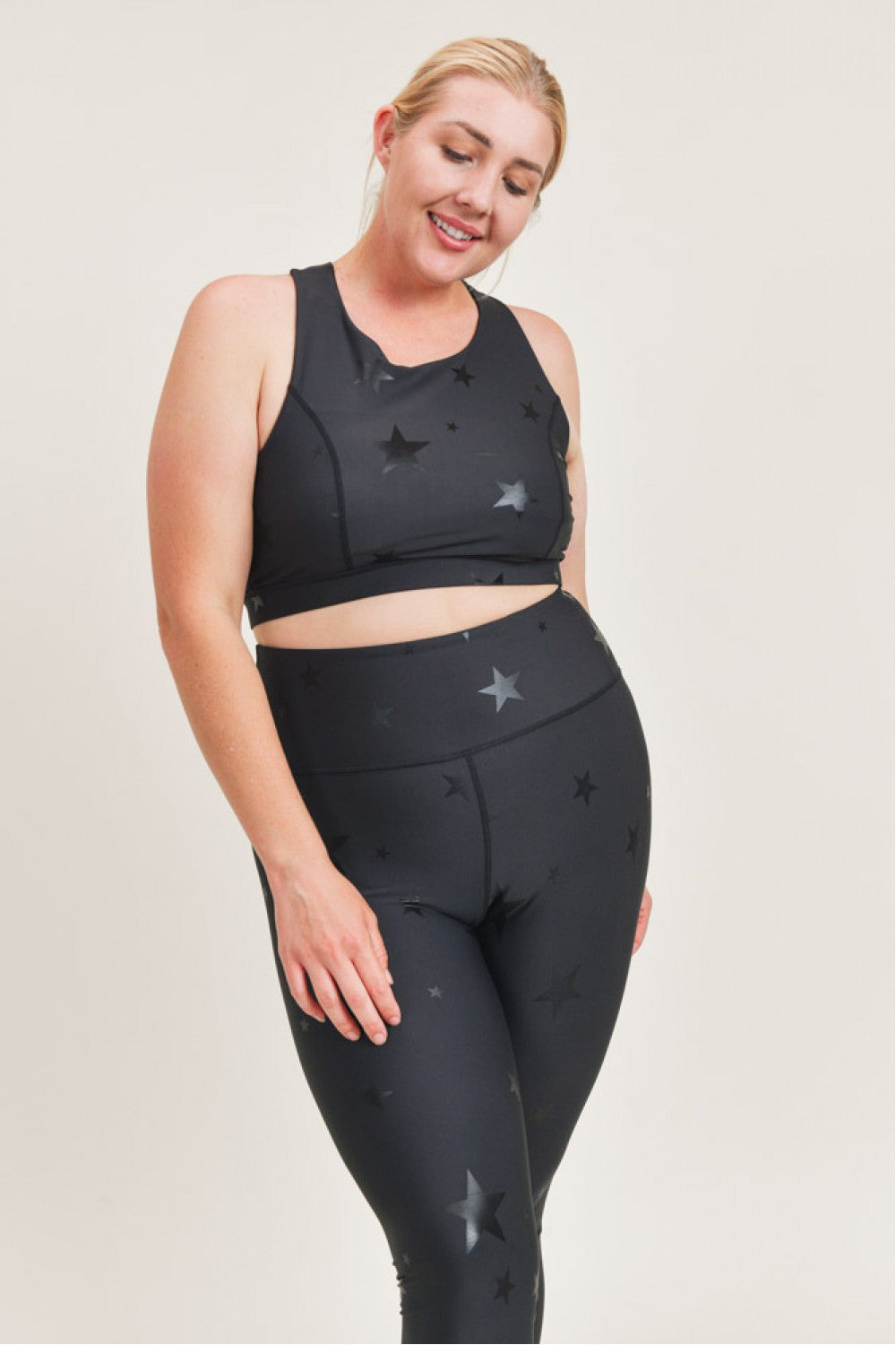 Woman wearing a black sports bra and leggings with star patterns on a plain background