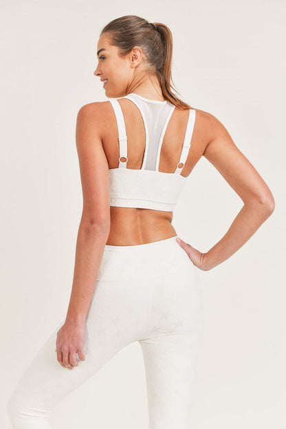 Woman wearing a white sports bra and leggings on a light gray background