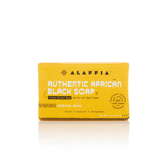 Alaffia Authentic African Black Soap Charcoal Reishi bar soap in a yellow cardboard box, shown on a white background with a soft reflection.
