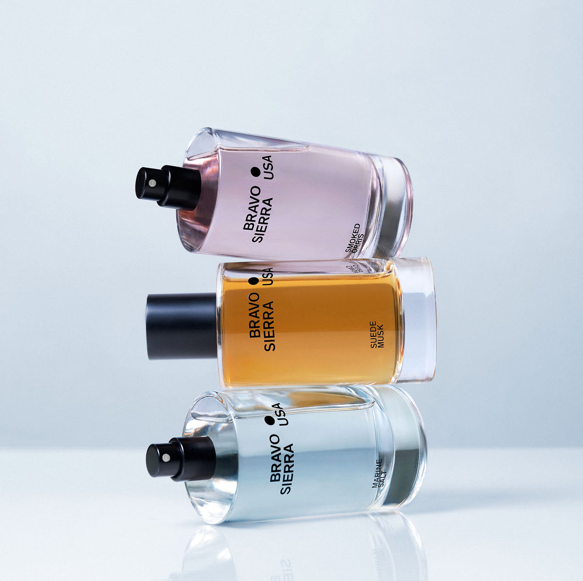Three Bravo Sierra USA perfume bottles stacked on a reflective surface with a light blue gradient background.