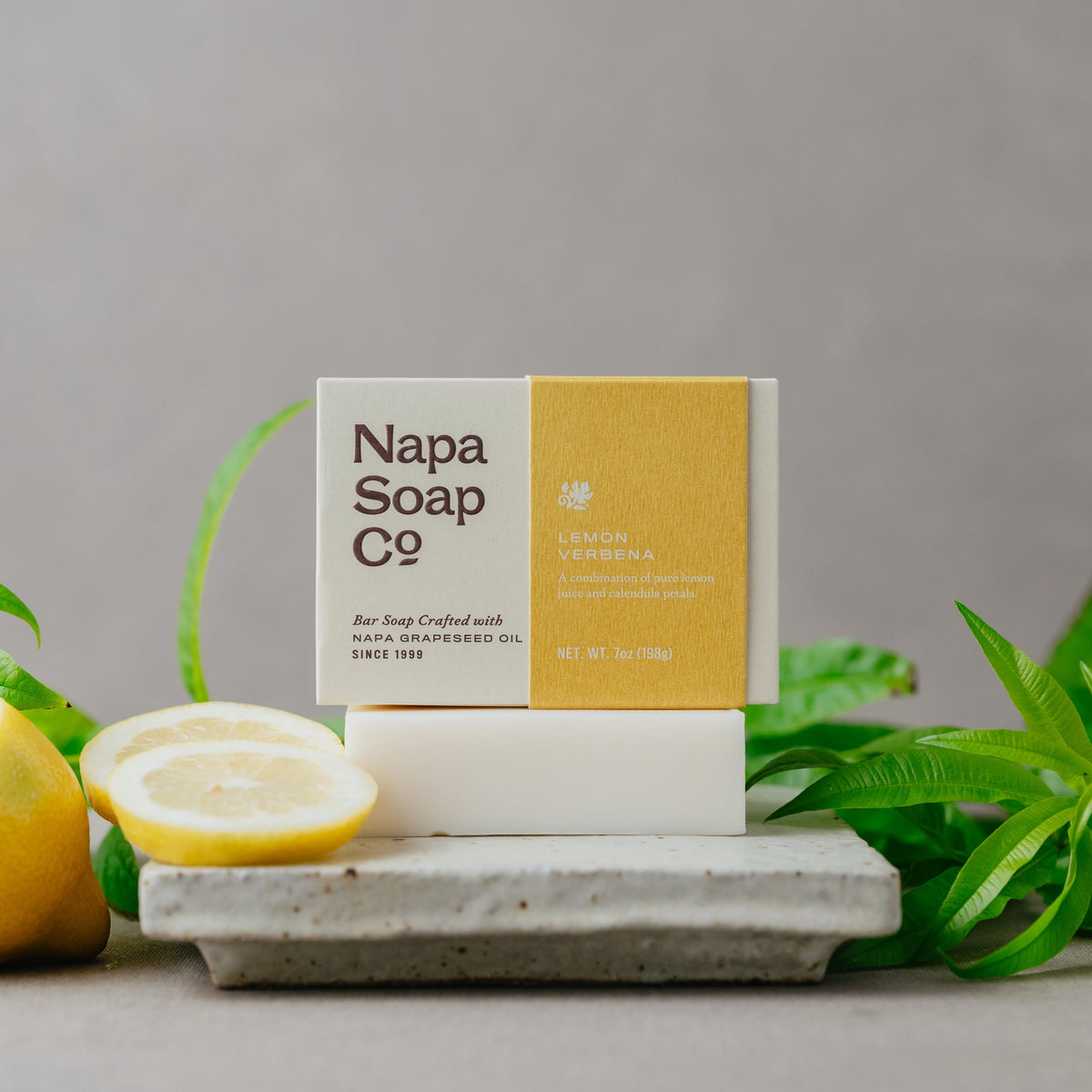 Napa Soap Co. bar soap on a white stand with lemons and greenery on a gray background