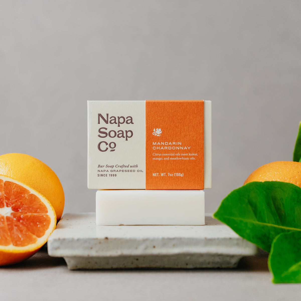 Napa Soap Co. soap bar with packaging on a gray surface with oranges and leaves.