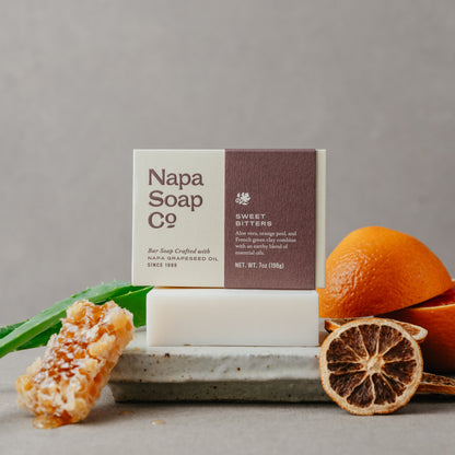 Napa Soap Co bar soap with packaging, oranges, and honeycomb on a gray background