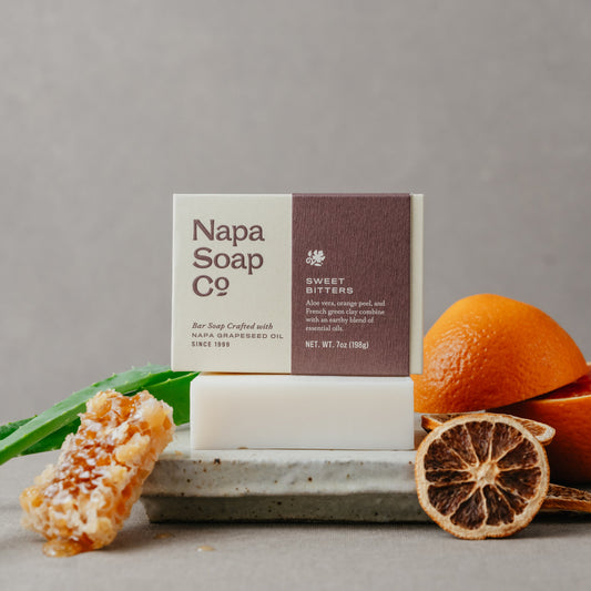 Napa Soap Co bar soap with packaging, oranges, and honeycomb on a gray background