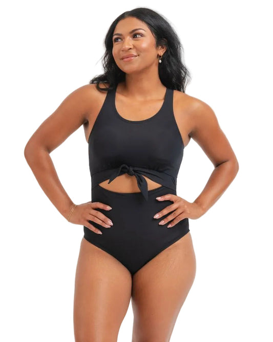 A woman modeling a black one-piece swimsuit with a halter-style neckline, side cutout, and front tie detail, photographed against a plain white background.