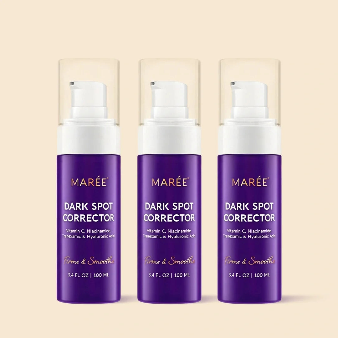 Three MARÉE Dark Spot Corrector pump bottles in a row on a warm beige background. The bottles are deep purple with white pump tops and clear protective caps, featuring gold and white text.