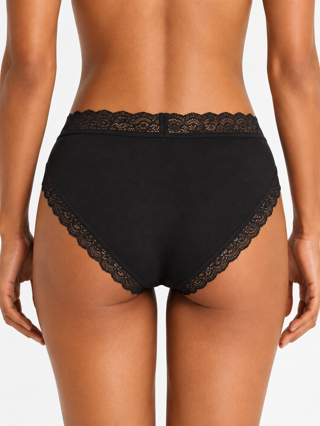 Rear view of a model wearing black high-waisted underwear with black lace trim on the waistband and leg openings, set against a plain light gray studio background.