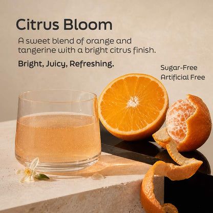 A glass of pale orange citrus drink beside a halved orange, peeled orange segments, and orange zest on a beige surface, with text reading 'Citrus Bloom' and flavor/quality claims.