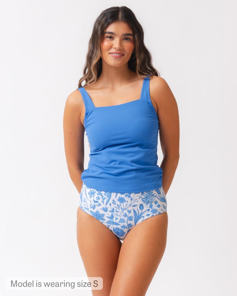 Woman wearing a blue tankini with floral patterned bottoms on a white background