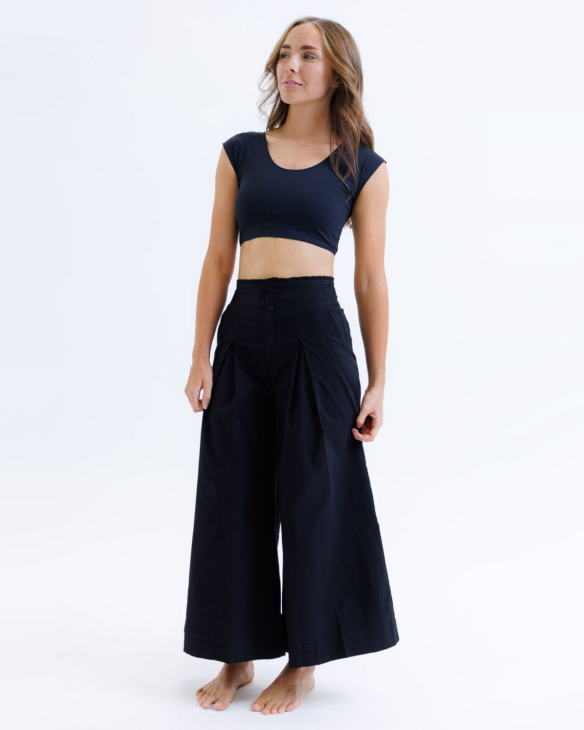 Woman wearing a black crop top and wide-leg pants on a white background
