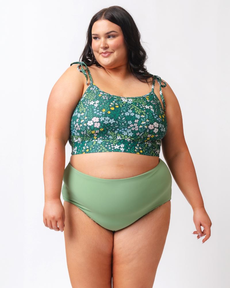 Woman wearing a green floral bikini top and green high-waisted bottoms on a white background
