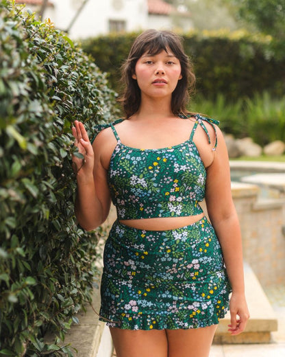 Woman wearing a green floral dress standing outdoors next to a bush.