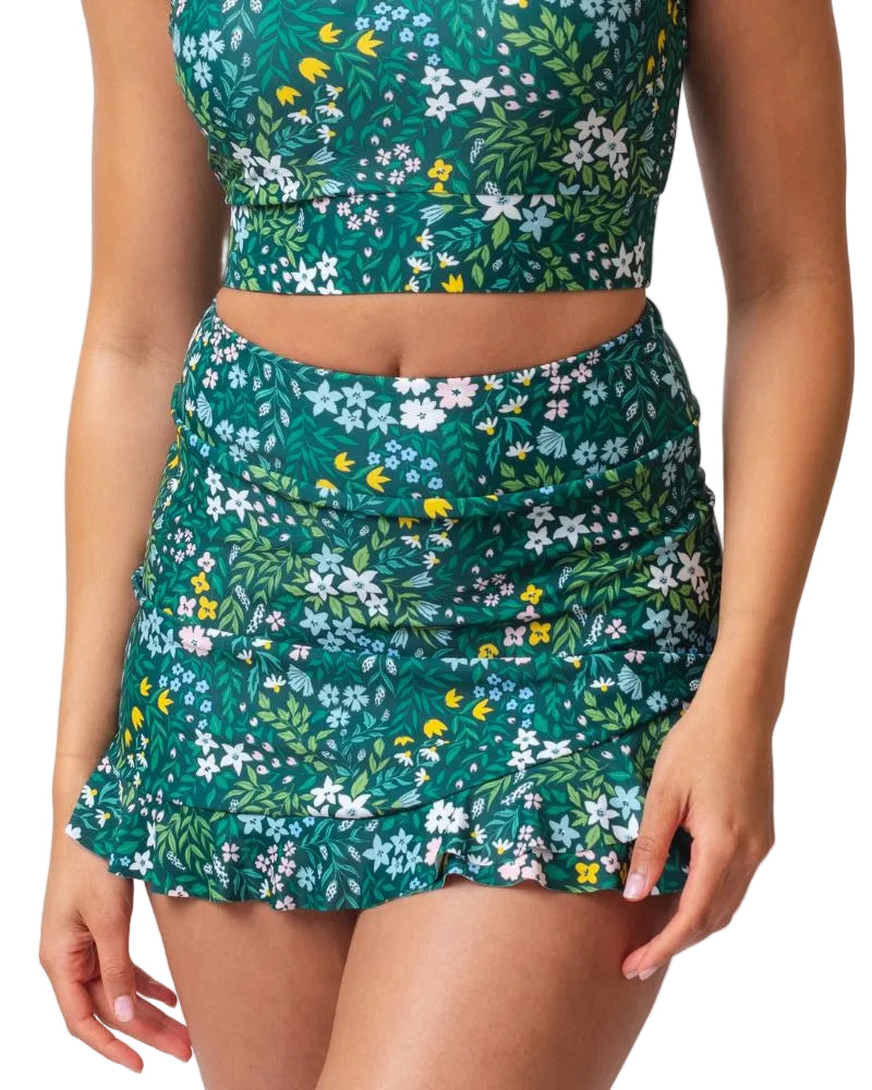 A model wearing a matching two-piece swimsuit featuring a green tropical floral print with white, yellow, and blue flowers, set against a plain white background.