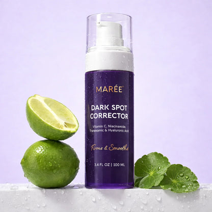 A bottle of MARÉE Dark Spot Corrector shown upright on a white surface with limes and green leaves against a light lavender background. The product bottle is purple with a white pump and clear cap, and the scene includes fresh lime halves and water droplets.