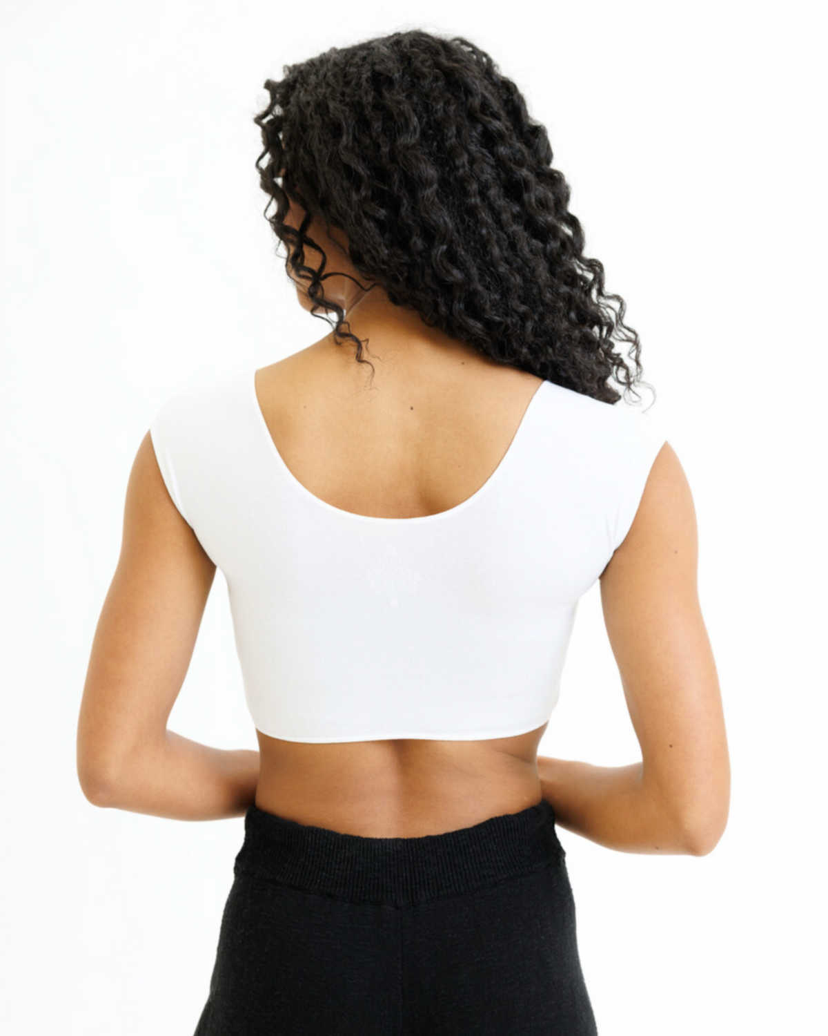 Person wearing a white crop top and black pants on a white background