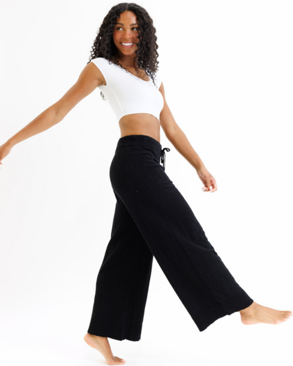 Woman wearing a white crop top and black wide-leg pants on a white background