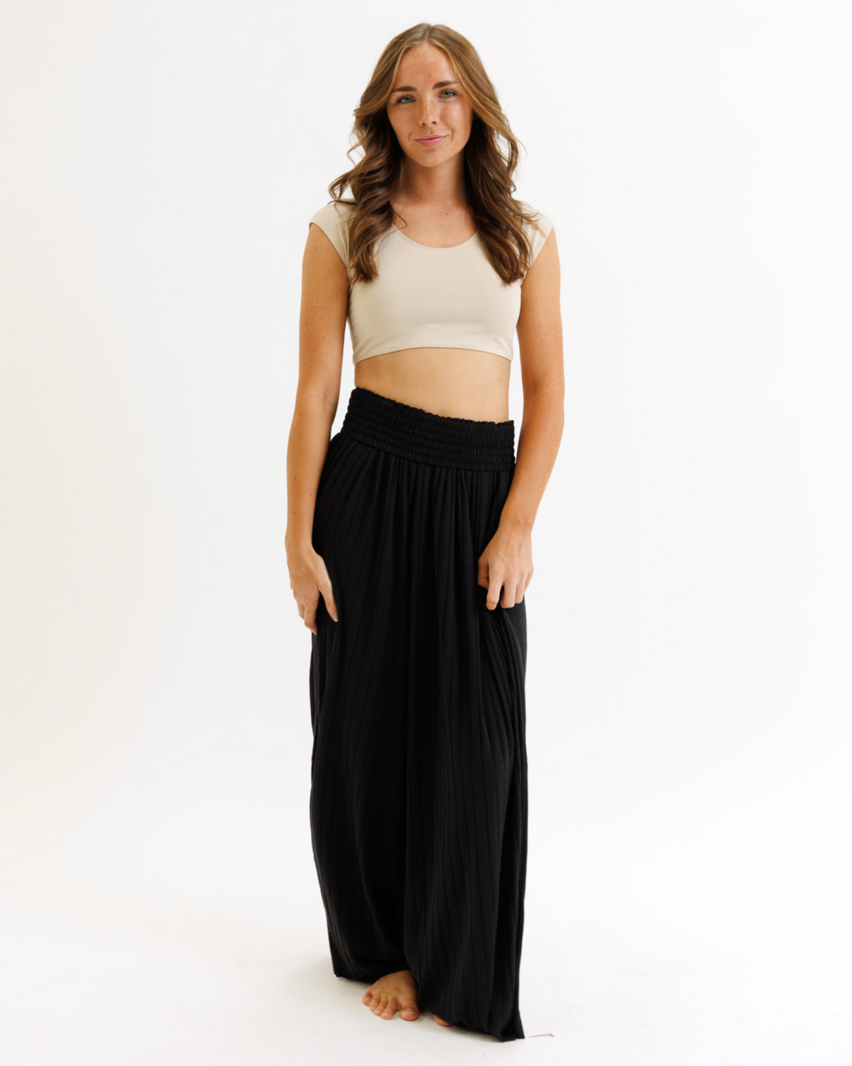Woman wearing a beige crop top and black flowing pants on a white background