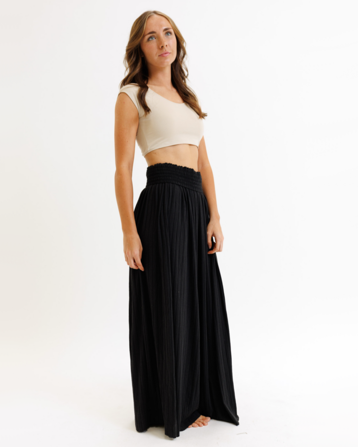 Woman wearing a white crop top and black flowing pants on a white background