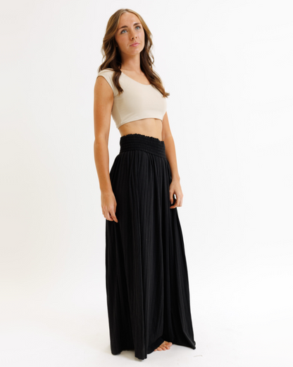 Woman wearing a white crop top and black flowing pants on a white background