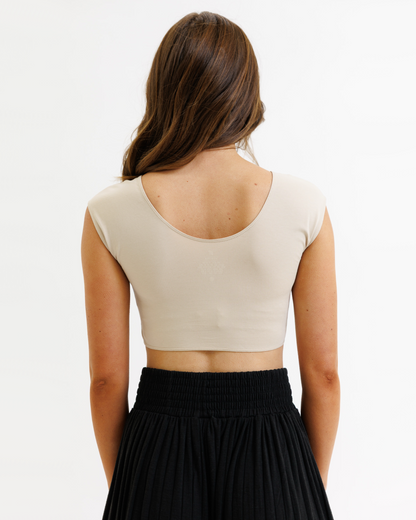 Woman wearing a beige crop top and black pleated skirt on a white background