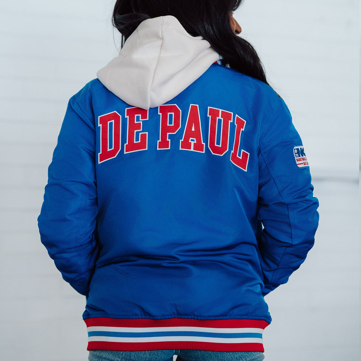 Blue jacket with 'DE PAUL' text on the back, worn by a person against a white background