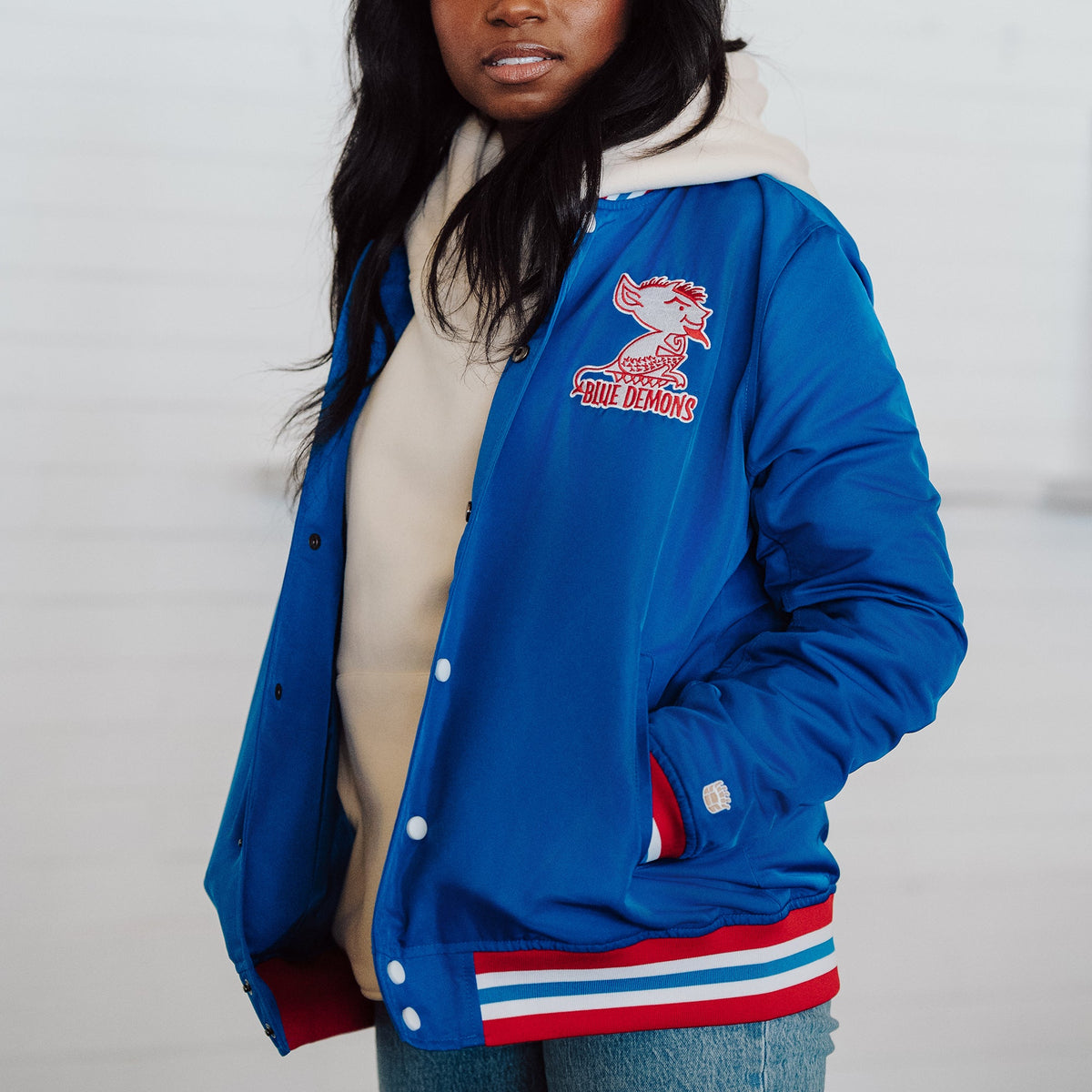 Person wearing a blue letterman jacket with a logo on a plain background
