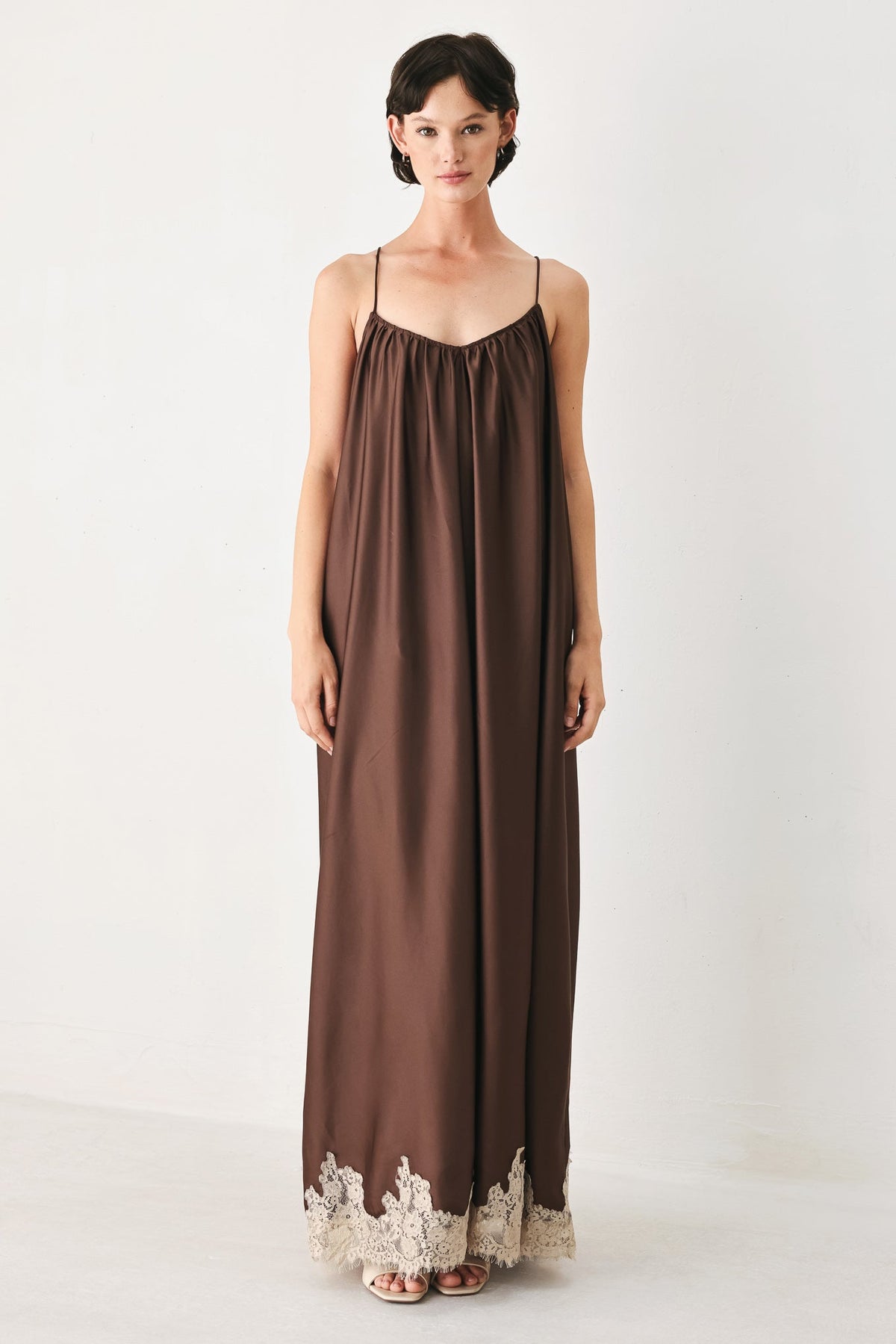 Woman wearing a brown slip dress with lace trim on a white background