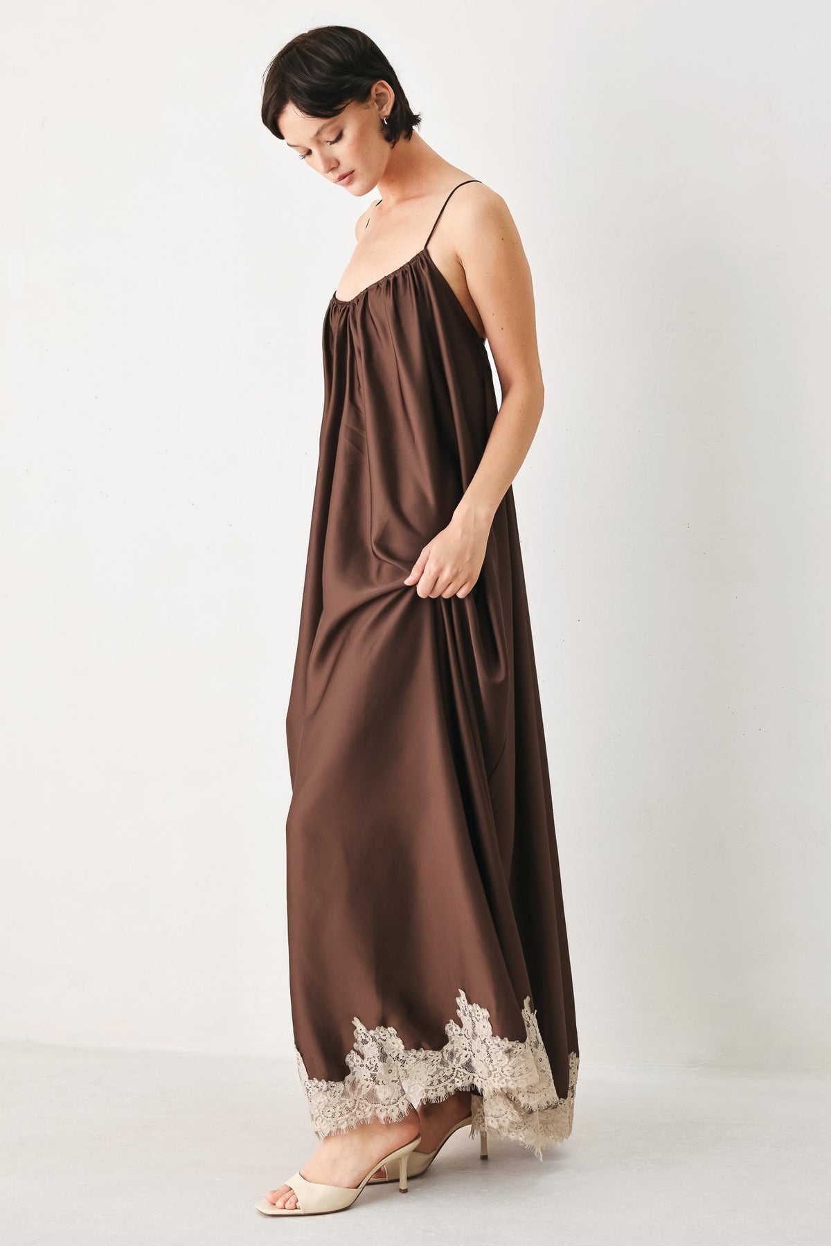 Woman wearing a brown slip dress with lace trim on a white background
