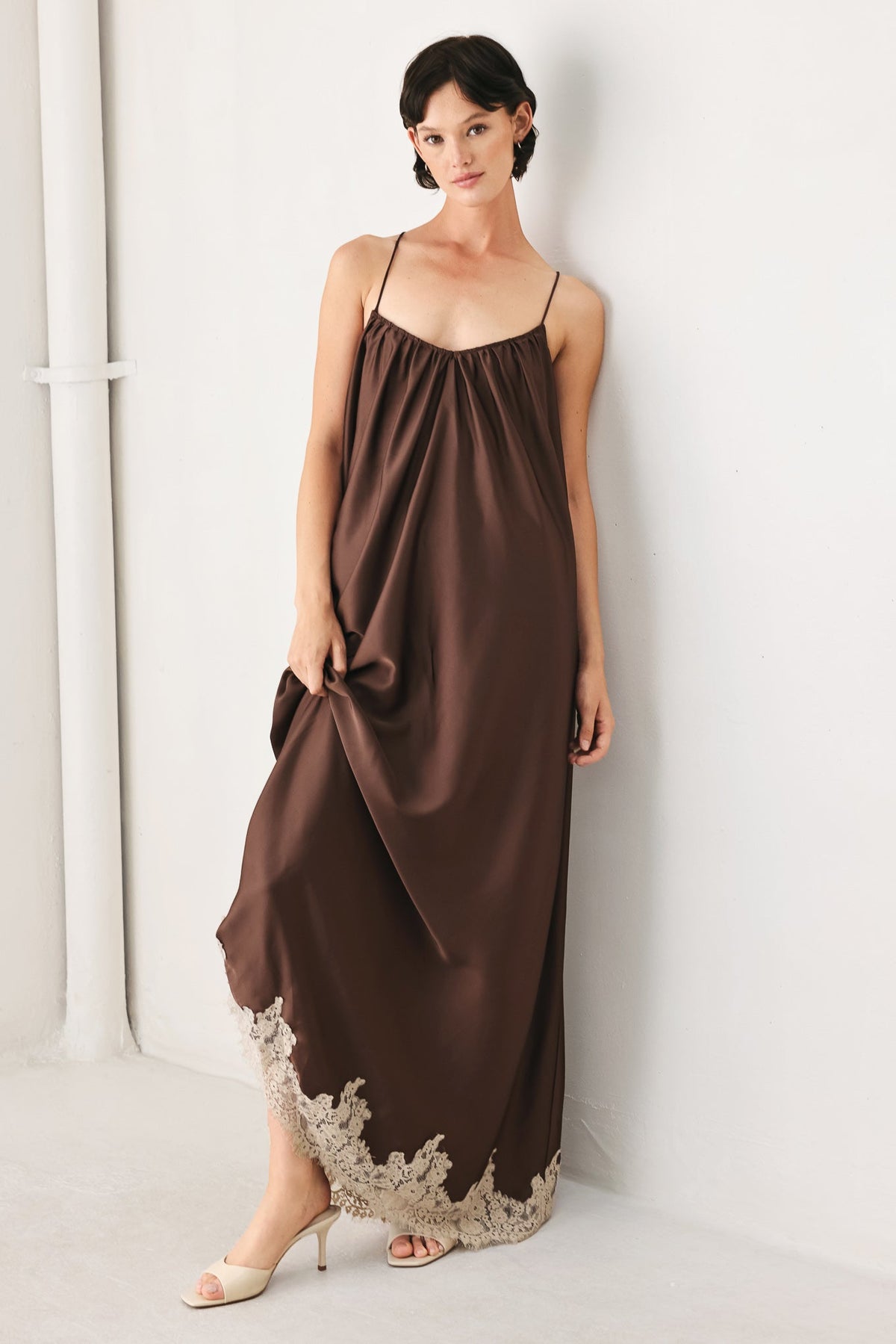 Woman wearing a brown slip dress with lace trim against a white background