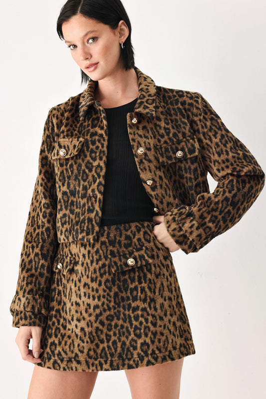 A model wearing a brown and black leopard print jacket and matching mini skirt over a black ribbed top, photographed against a plain white studio background.