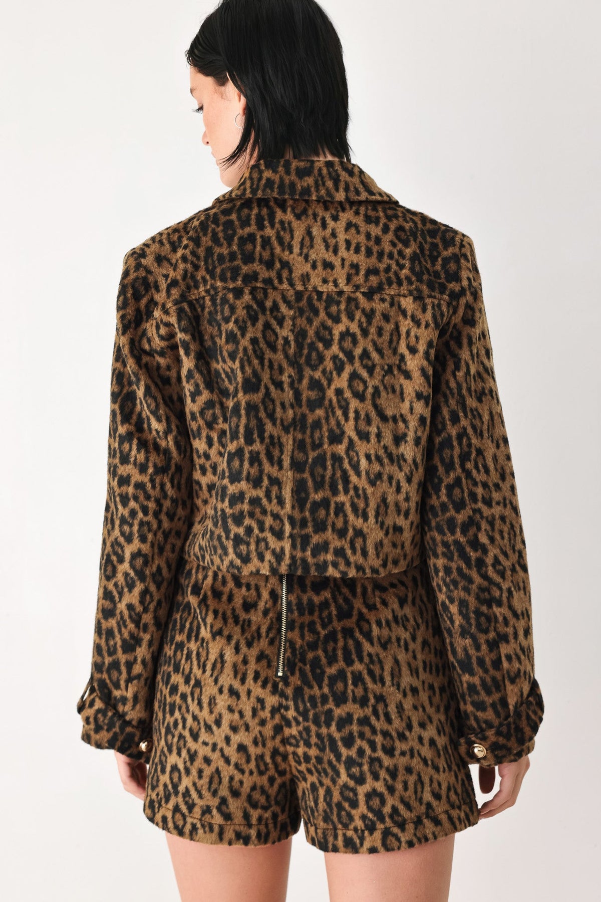 A model shown from the back wearing a matching leopard-print jacket and shorts set against a plain white studio background.