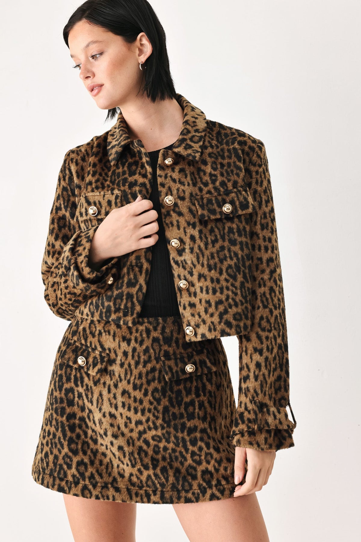 A model wearing a matching brown and black leopard print jacket and mini skirt set with gold-tone buttons, photographed against a plain light background.