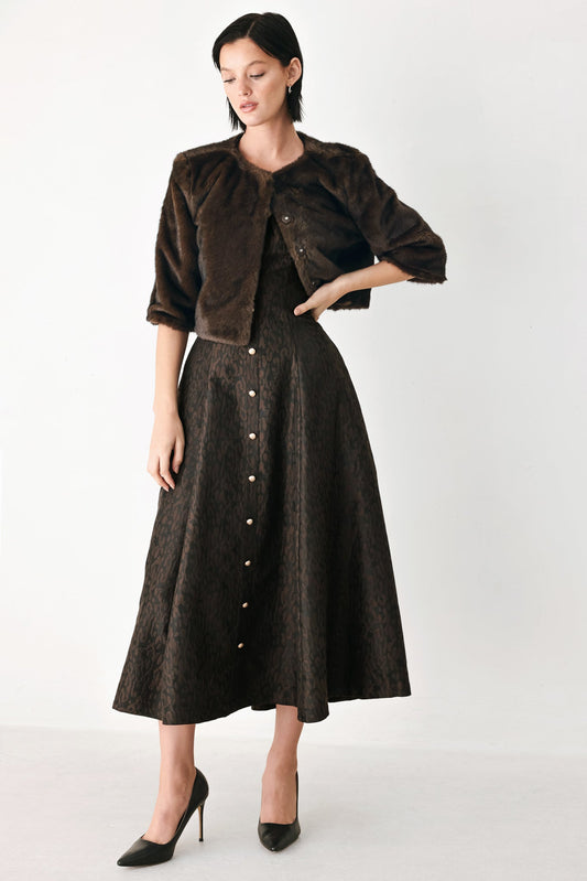 A model wearing a dark brown cropped jacket and matching dark brown button-front midi skirt, styled with black pointed-toe heels against a plain light gray studio background.