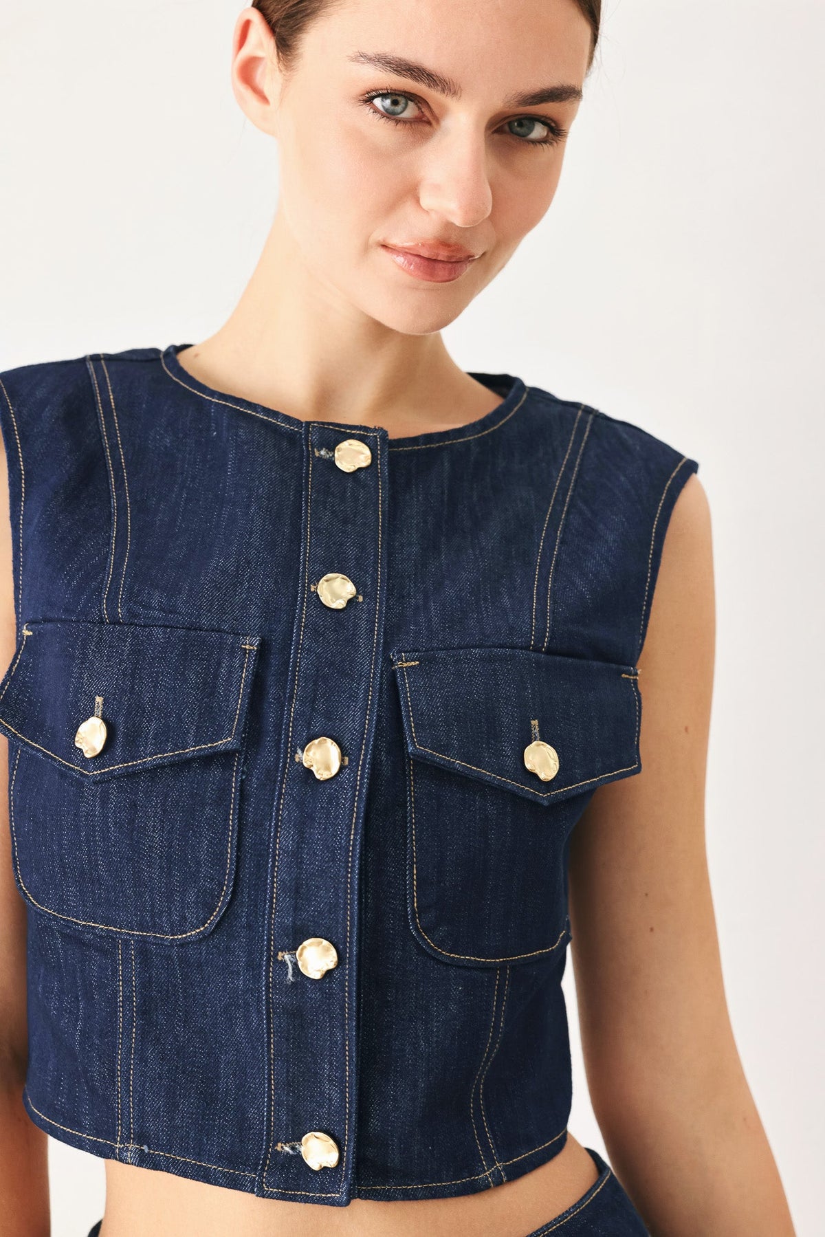 Cropped indigo denim vest with a button front, shown on a model against a plain studio background.