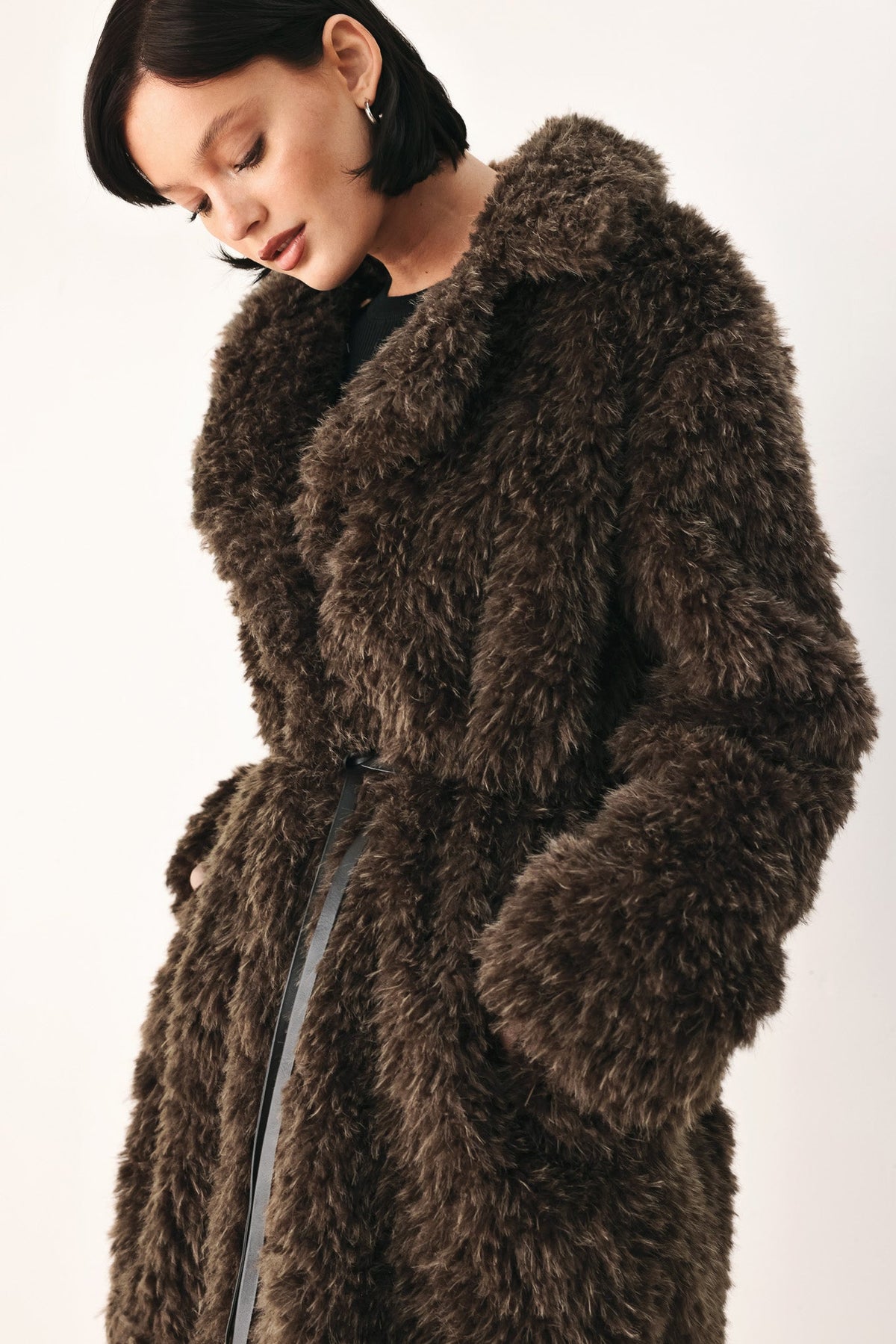 A model wearing a dark brown shaggy faux fur coat with a matching belt, photographed against a plain light background.