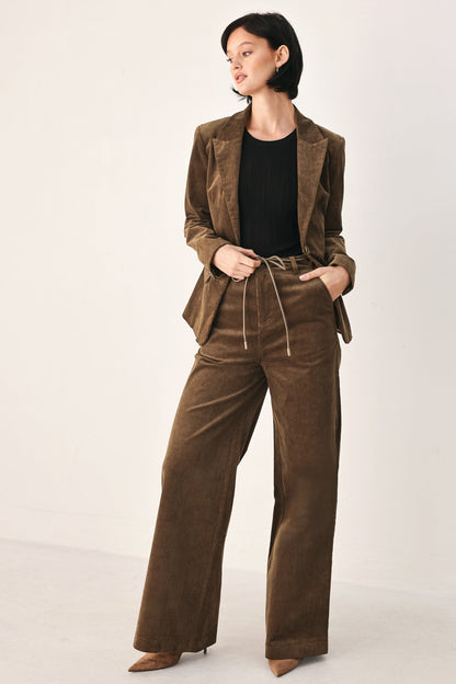 A model wearing a matching brown corduroy blazer and wide-leg trousers set with a drawstring waist, styled over a black top and brown pointed-toe heels, against a plain off-white studio background.