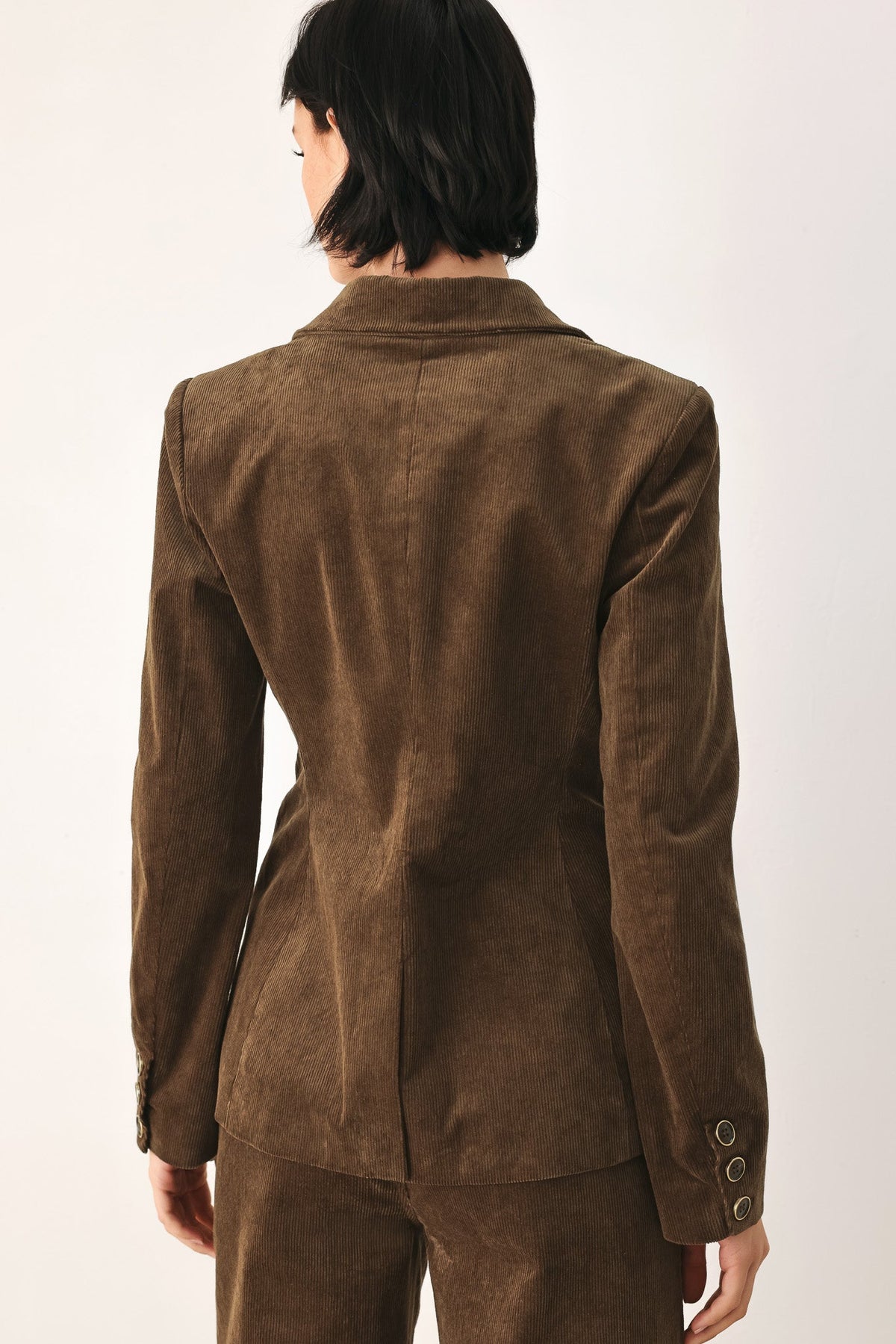 A person shown from the back wearing a brown suede or nubuck blazer with matching trousers against a plain light background.