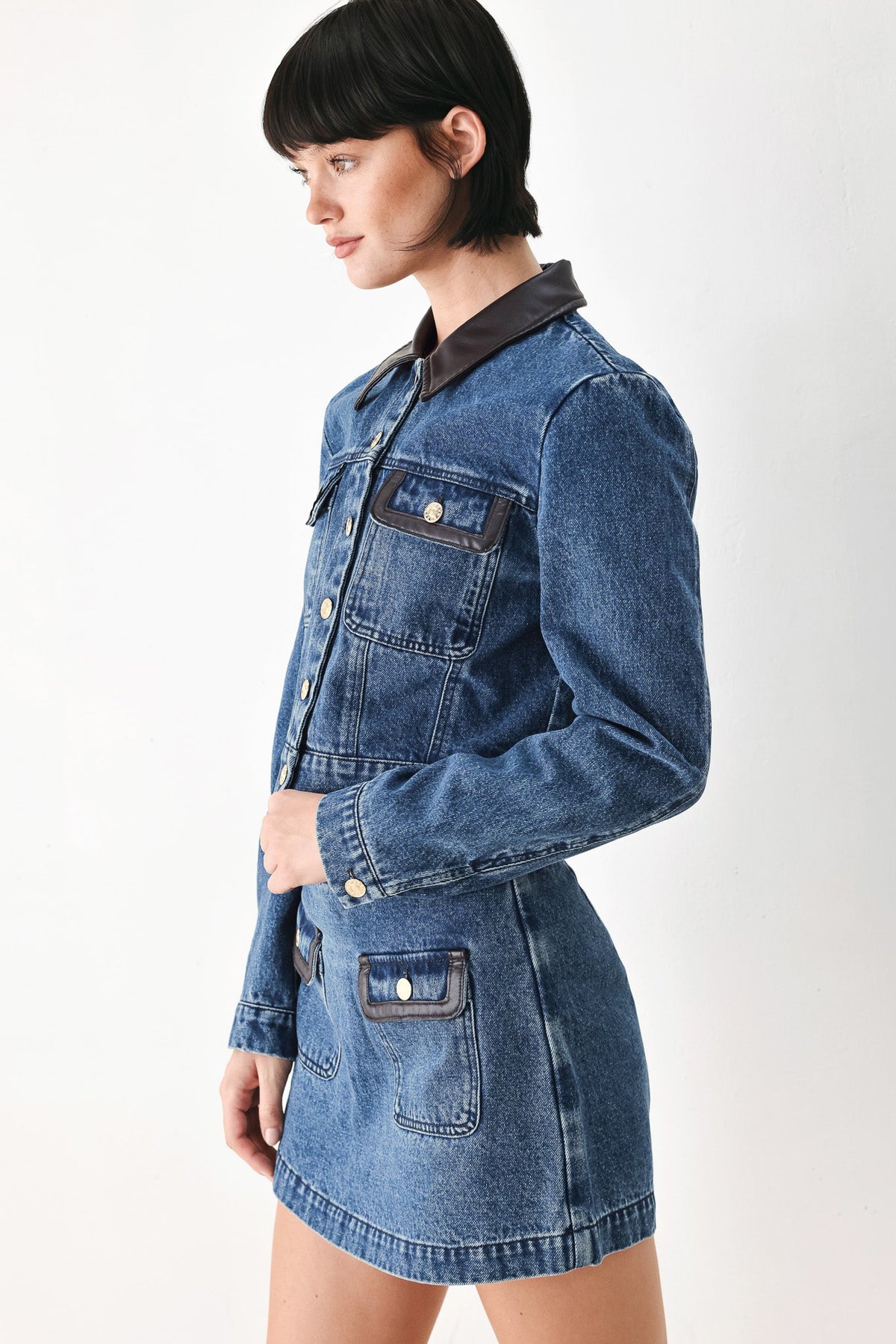 Contrast faux leather trim on the pockets of a washed denim cropped jacket.
