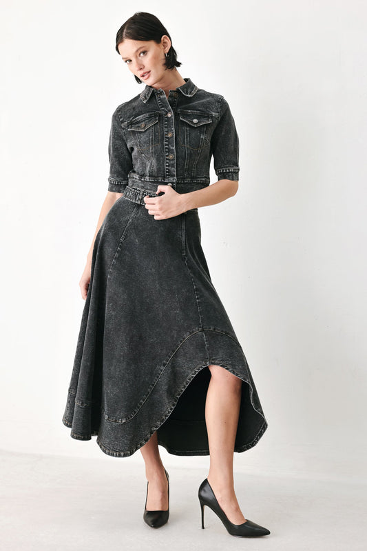 A model wearing a dark gray washed denim high-low dress with a button-up shirt collar, short sleeves, and a matching belt, paired with black heels, against a plain light gray background.