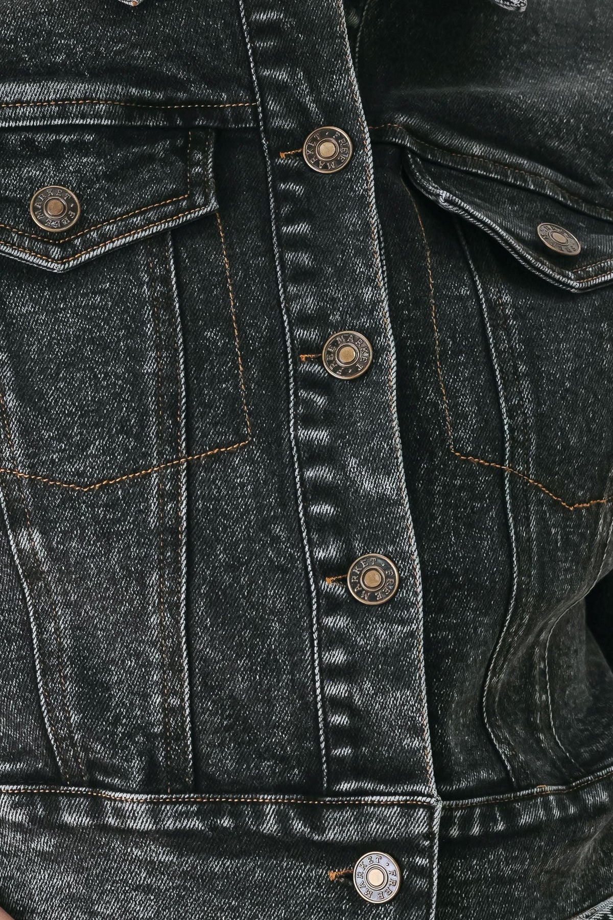 Close-up of a dark washed denim jacket showing the front button closure, chest pockets, and detailed denim texture.