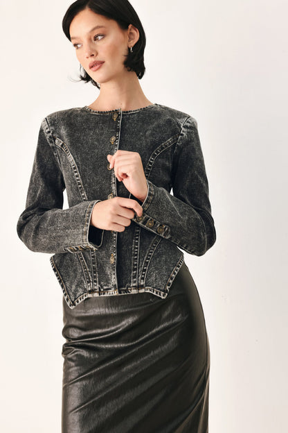 A woman wearing a cropped, long-sleeve dark gray acid-wash denim jacket with gold-tone buttons and a black faux-leather pencil skirt, photographed against a plain light background.
