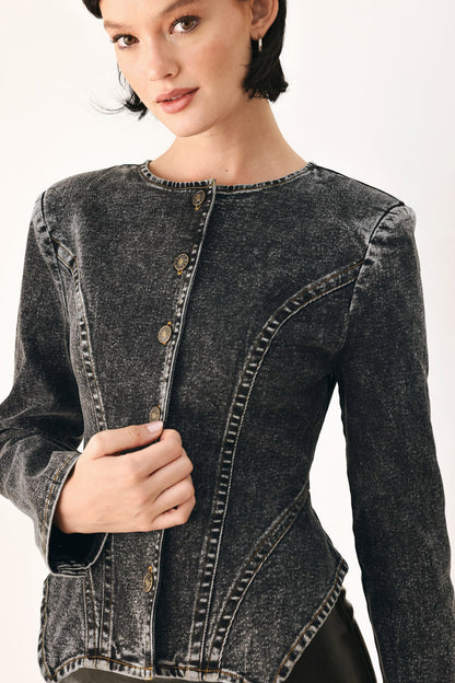 A close-up of a model wearing a dark gray mineral-wash denim jacket with button-front detailing and contrast stitching, set against a plain light background.