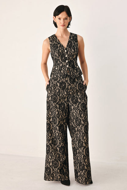 A woman modeling a sleeveless black lace jumpsuit with a V-neckline, front buttons, and wide legs, photographed against a plain light studio background.