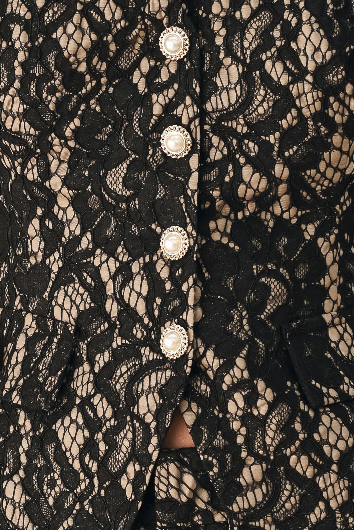 Close-up of a black lace garment with a floral lace pattern and a vertical row of decorative buttons with pearl-like centers.