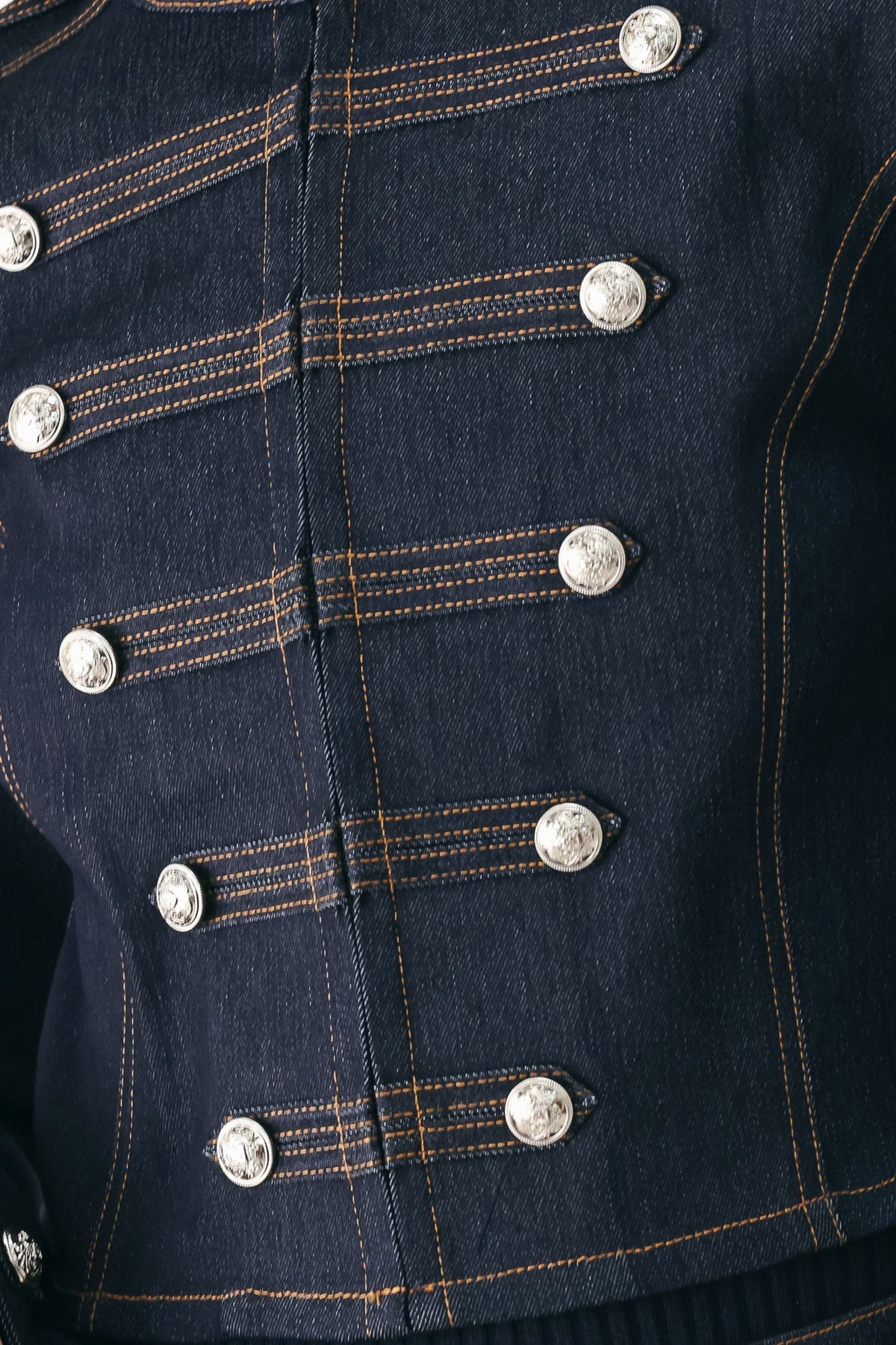Close-up of a dark navy blue denim jacket featuring double-breasted silver buttons and contrasting orange stitching.