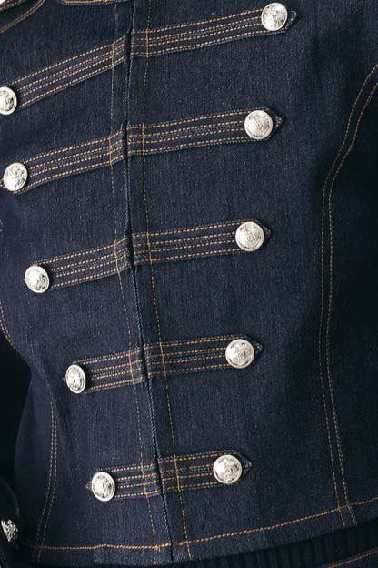Close-up of a dark navy blue denim jacket featuring double-breasted silver buttons and contrasting orange stitching.