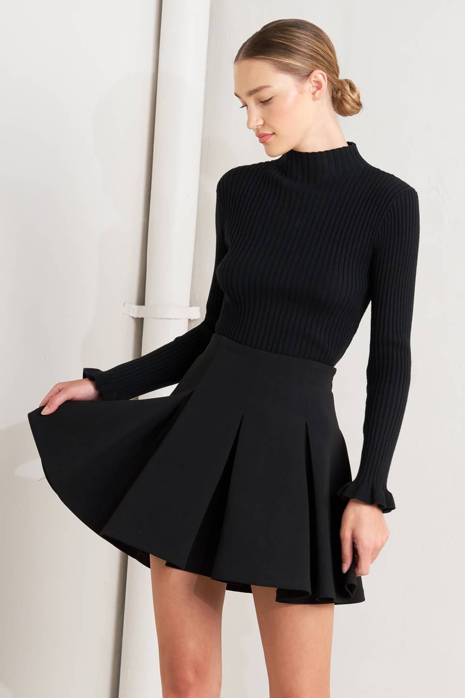 Woman wearing a black ribbed sweater and black skirt on a white background
