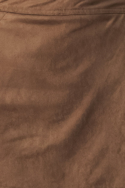A close-up of a brown suede or faux-suede fabric texture with soft folds and a stitched seam near the top.
