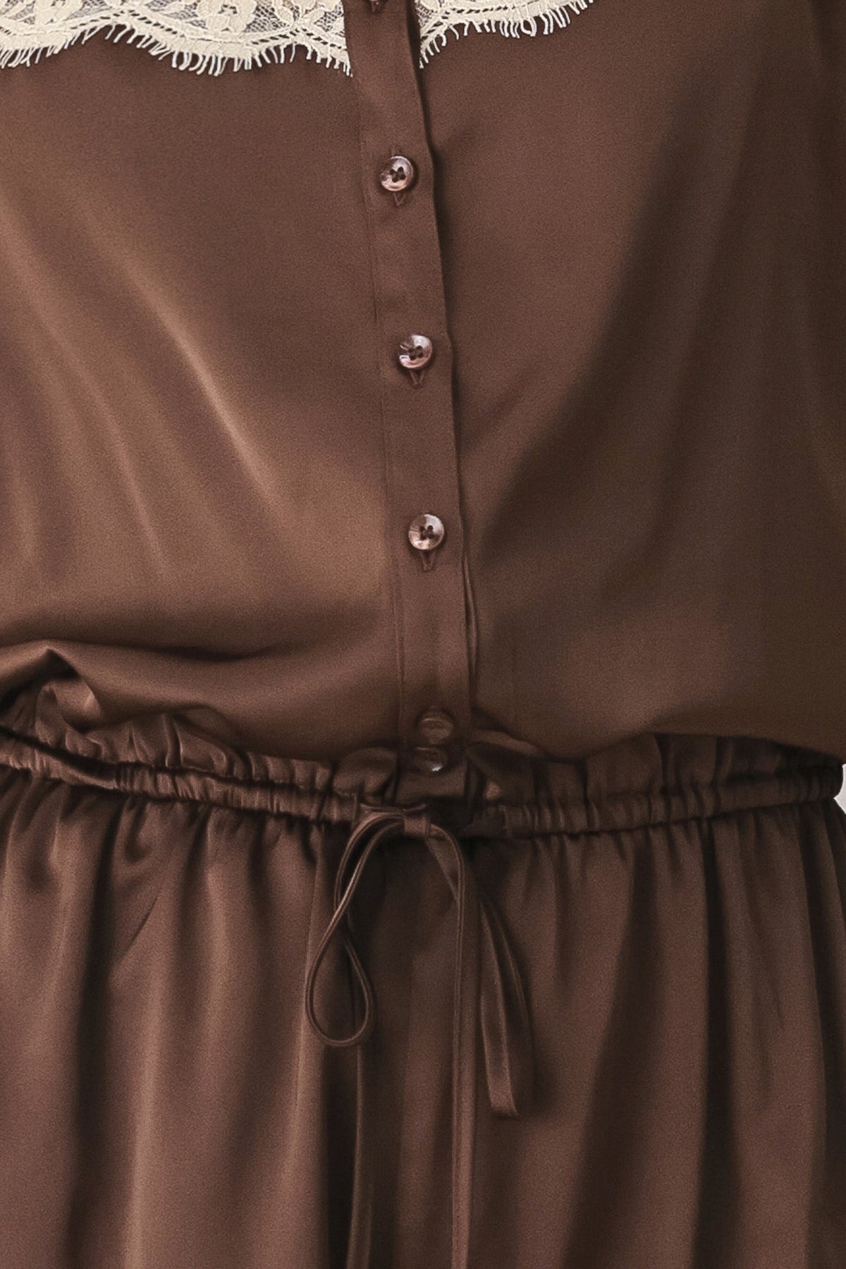 Close-up of a brown satin-like button-front garment with a lace collar and drawstring waist, cropped to show fabric texture and details.