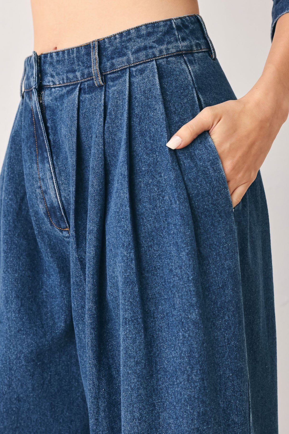 Full-length view of medium indigo wide-leg denim pants with front pleats and side pockets.